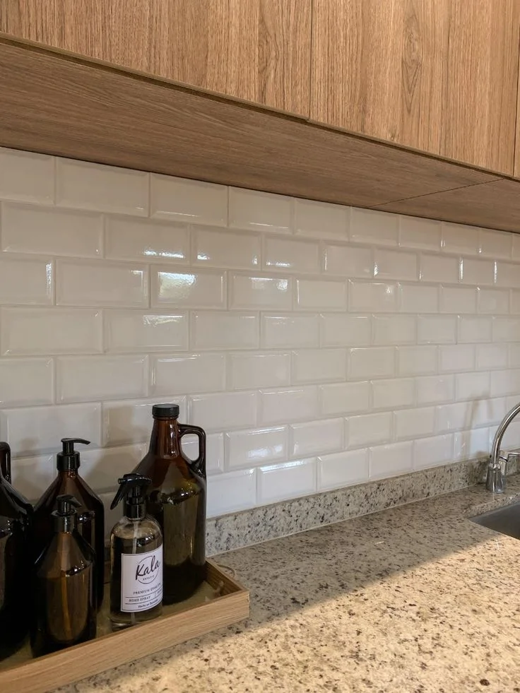 Cream beveled subway tile kitchen backsplash paired with warm wood upper cabinets and granite countertop