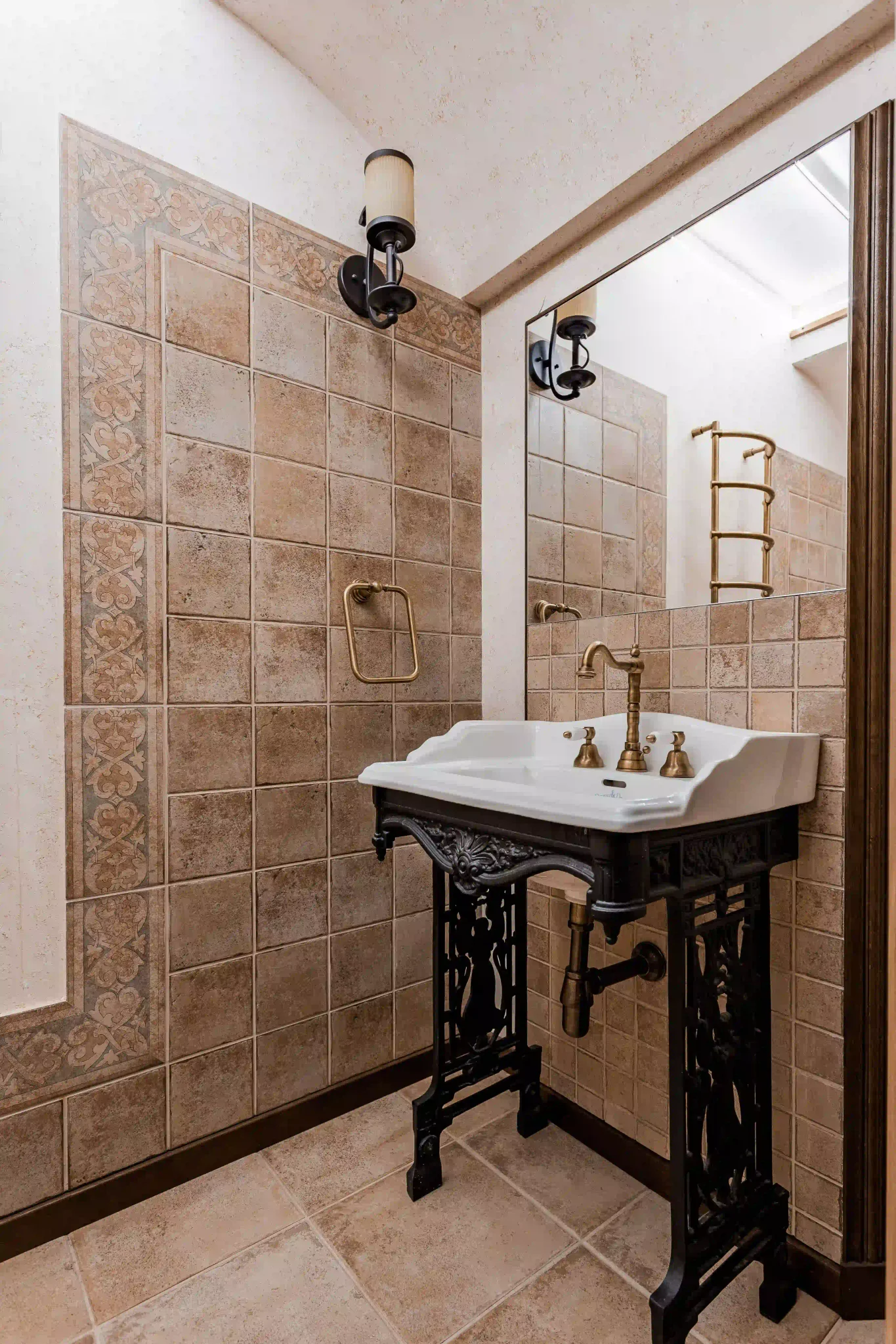 Rustic bathroom with terracotta square wall tiles, decorative border, and ornate pedestal sink